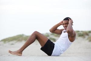 gesunder junger Mann, der Sit-Ups am Strand tut
