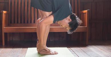 sportlicher asiatischer mann in schwarz macht yoga, während er zu hause auf yogamatte mit holzboden trainiert. mann yoga praxis pose training gesundes lebenskonzept foto