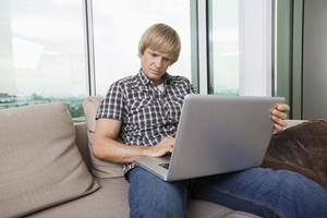 ernsthafter Mann im mittleren Erwachsenenalter, der Laptop auf Sofa zu Hause benutzt
