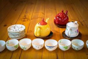 Gelbe, weiße und rote Teekanne auf dem Holztisch mit weißer Schale und Tasse in der ersten Reihe. foto