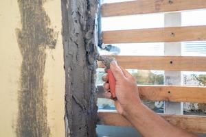 Nahaufnahme Die Hand eines asiatischen Mannes hält eine Kelle, um die Wand mit frischem Zement mit Holzlatten daneben zu reparieren und zu dekorieren foto