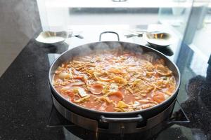 tokboki koreanisches traditionelles essen heißer und würziger reiskuchen, kombination und puff mit käse und gemüse auf dem schwarzen tisch auftragen foto