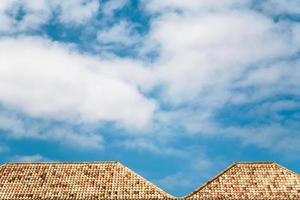 weiße Wolken am blauen Himmel über orangefarbenen Ziegeldächern foto