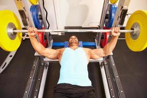 Mann, der Muskeln beim Bankdrücken von Gewichten in einem Fitnessstudio biegt foto