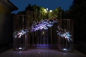 moderner Hochzeitsbogen aus Metallkupferstäben und frischen Blumen bei Nacht mit beleuchteten Laternen. foto