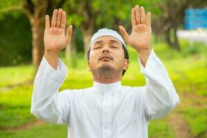 asiatischer muslimischer mann betet allah, gott des islams, während er die arme erhebt foto