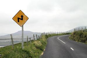 Warnung - gelbes Verkehrsschild, das eine gefährliche Kurve voraus ankündigt foto