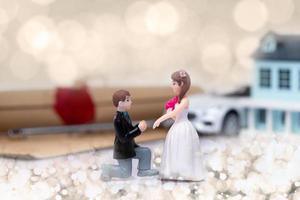 kleine Miniaturpuppe von Liebespaaren schlägt für die Ehe mit romantischem Valentinsmoment mit Hintergrund des Dokumentvermögenshaus-Autofahrzeugs vor, Metapherkonzept-Handelsliebesgeld foto