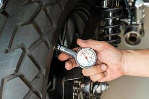 mann, der manometer hält, um motorradreifendruck, wartung, reparaturmotorradkonzept in der garage zu prüfen. selektiver fokus foto