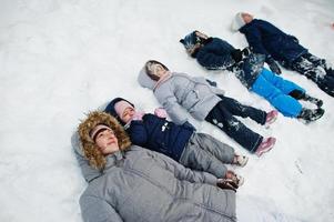 mutter mit vier kindern in der winternatur, die im schnee liegt. foto