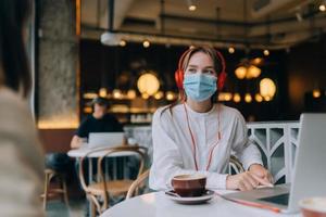 Ein Mädchen, das mit Kopfhörern in einem Café sitzt. Ausbruch Coronavirus. foto
