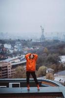 Mädchen in einer orangefarbenen Jacke posiert auf dem Dach eines Gebäudes im Stadtzentrum foto