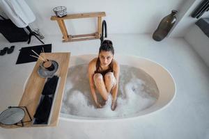 junge Frau umarmt ihre Beine, während sie in der Badewanne sitzt foto