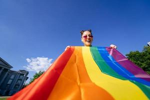 Eine junge Frau entwickelt eine Regenbogenfahne gegen den Himmel foto