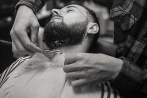 junger bärtiger mann, der vom friseur im friseursalon rasiert wird foto