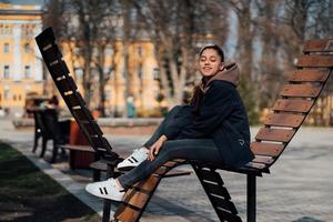 junge Frau sitzt auf einer Bank im Park, lächelt und schaut in die Kamera foto