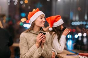 Mädchen mit Weihnachtsmütze sitzt im Café und trinkt Kaffee foto