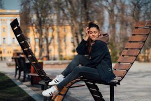 junge Frau sitzt auf einer Bank im Park, lächelt und schaut in die Kamera foto