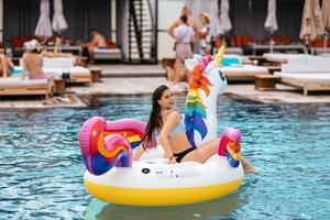 Frau auf aufblasbarer Einhorn-Spielzeugmatratze schwimmt im Pool. foto