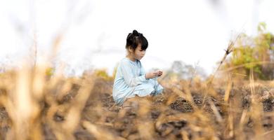 süßes kleines Mädchen, das auf dem Gras im Wald hinter dem brennenden Gras sitzt foto