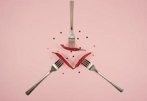 Auf einem rosa Tisch liegen Gabeln mit roten Peperoni und Konfetti in Form des Herzens foto