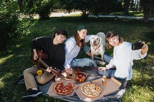 Gesellschaft von schönen jungen Leuten und Hunden, die ein Mittagessen im Freien haben. foto