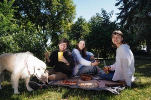 Gesellschaft von schönen jungen Leuten und Hunden, die ein Mittagessen im Freien haben. foto