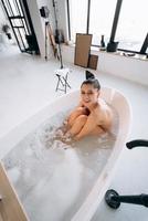 junge Frau umarmt ihre Beine, während sie in der Badewanne sitzt foto