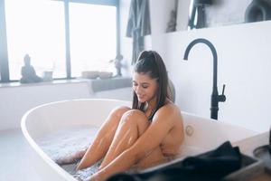 junge Frau umarmt ihre Beine, während sie in der Badewanne sitzt foto