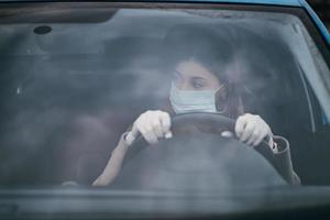 junge frau in einer maske und handschuhen, die ein auto fahren. foto