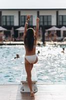 junge Frau auf dem Hintergrund des Pools in einem weißen Badeanzug. foto
