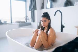 junge Frau umarmt ihre Beine, während sie in der Badewanne sitzt foto