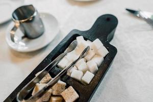 Schüssel mit weißen und braunen Zuckerwürfeln und mit einer Zuckerzange. foto