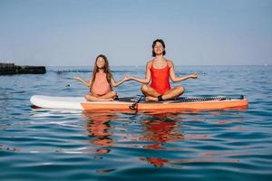 mutter und kleine tochter machen yoga auf dem paddelbrett foto