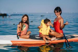 mutter und zwei kleine tochter machen yoga auf dem paddelbrett foto