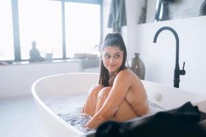 junge Frau umarmt ihre Beine, während sie in der Badewanne sitzt foto