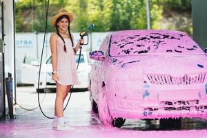frau mit schlauch steht neben dem auto, das mit rosa schaum bedeckt ist foto