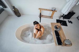 junge Frau umarmt ihre Beine, während sie in der Badewanne sitzt foto