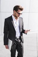 männlicher Geschäftsmann oder Arbeiter im schwarzen Anzug mit Smartphone foto