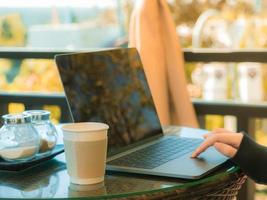 Geschäfts- und Kaffeepausenkonzept vom Freiberufler, der mit Computer-Laptop arbeitet und Kaffee am Morgencafé im Freien mit Weichzeichnerhintergrund trinkt foto