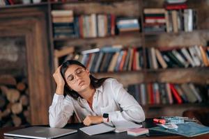 junge Frau im Büro, die über Probleme auf dem Hintergrund von Bücherregalen nachdenkt foto