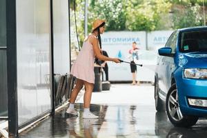 Brünette aus einem Hochdruckschlauch wäscht das Auto foto