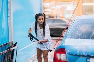 brünette aus einem hochdruckschlauch wäscht das auto in einer autowaschanlage foto