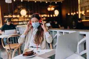 Ein Mädchen, das mit Kopfhörern in einem Café sitzt. Ausbruch Coronavirus. foto