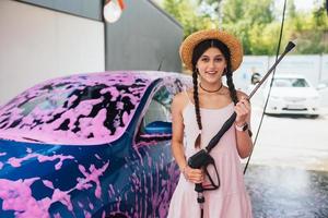 frau mit schlauch steht neben dem auto, das mit rosa schaum bedeckt ist foto