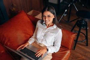 junge Frau sitzt auf einem roten Sofa, während sie an einem Laptop arbeitet. foto