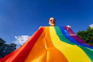 Eine junge Frau entwickelt eine Regenbogenfahne gegen den Himmel foto