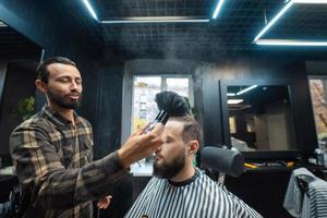 Der Meister entfernt die verbleibenden Haare des Kunden mit einer Bürste foto