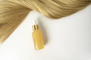 Ein natürliches ätherisches Öl oder Serum zur Haarpflege mit Vitamin C, das auf einem weißen Tisch liegt. haarpflege- und glättungskonzept foto