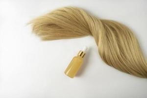 ein natürliches Öl oder Serum für die Haarpflege und eine Lage blondes Haar, die auf weißem Hintergrund liegt foto